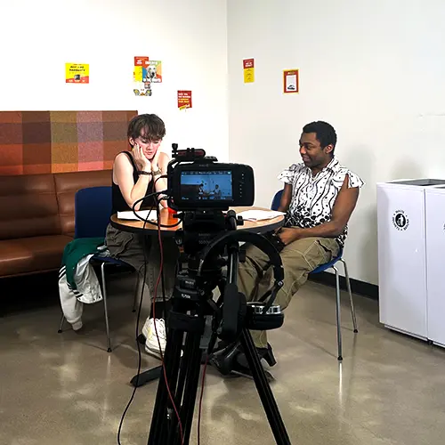 two students acting in a scene with a camera in the foreground.