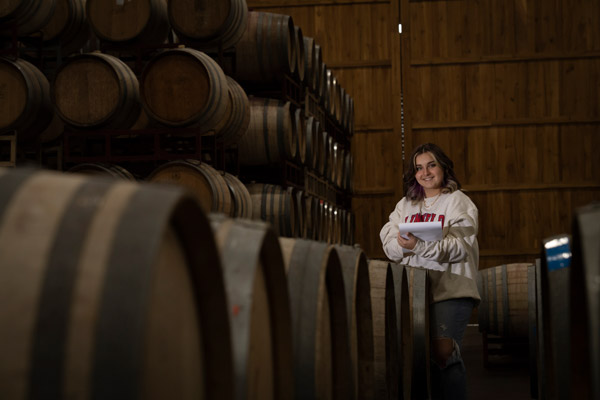 Emma taking notes at a winery surrounded by wine barrels 