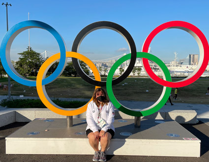 Stacey sitting in front of a five-Olympic ring figure in Tokyo