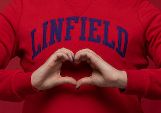 student holding hands in the shape of a heart wearing a Linfield sweatshirt