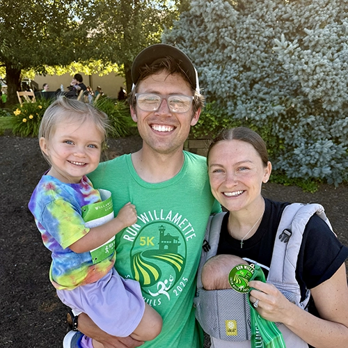 Alex and Kelsey posing for a photo after a race while holding their two kids.
