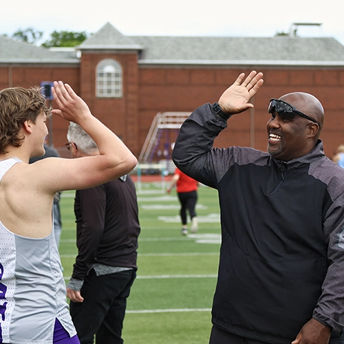 Tramaine giving a high five to a student athlete at a track meet.