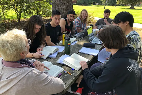 students sitting around a picnic table during an outdoor class.