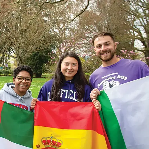 three students holding flags from the countries where they studied abroad.