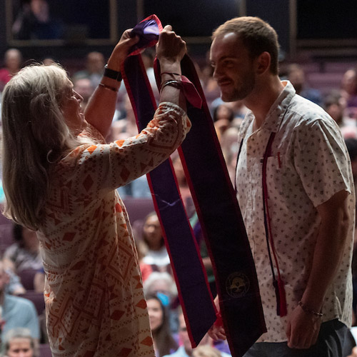 a nursing graduate receives his pin from a relative on stage