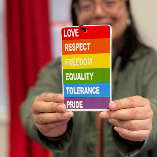 Student holding a plaque that says love, respect, freedom, equality, tolerance, pride in rainbow colors.