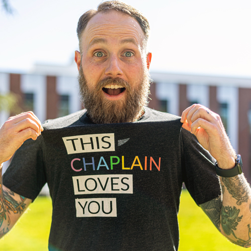 Linfield's chaplain wearing a t-shirt that says "This chaplain loves you" in rainbow colors.
