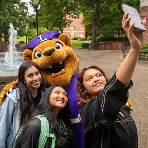 Three female students taking a selfie with Mack the Wildcat.