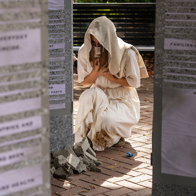 An art installation at Ground Zero: 2021 with a woman crying on her knees in front of pillars with the names of those lost during the attacks of 9/11.
