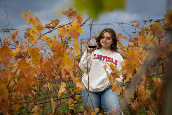 Linfield student holding a glass of red wine in a vineyard.