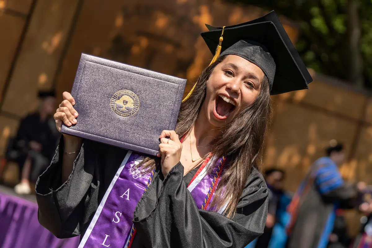 A graduate in cap and gown smiles with their diploma