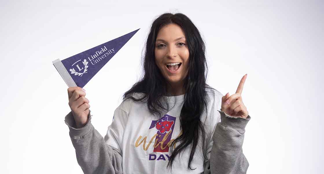 Female student proudly wearing a Linfield t-shirt and holding a Linfield pennant.