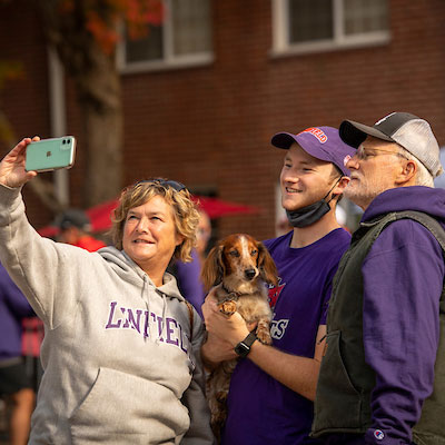 Male student holding his dog while posing for a picture with his mom and dad