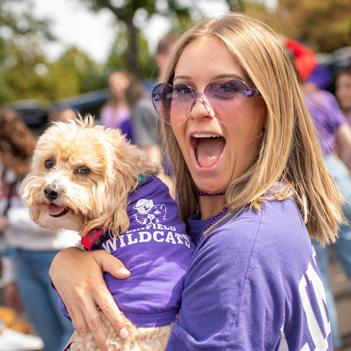 female student holding her dog, both in Linfield t-shirts