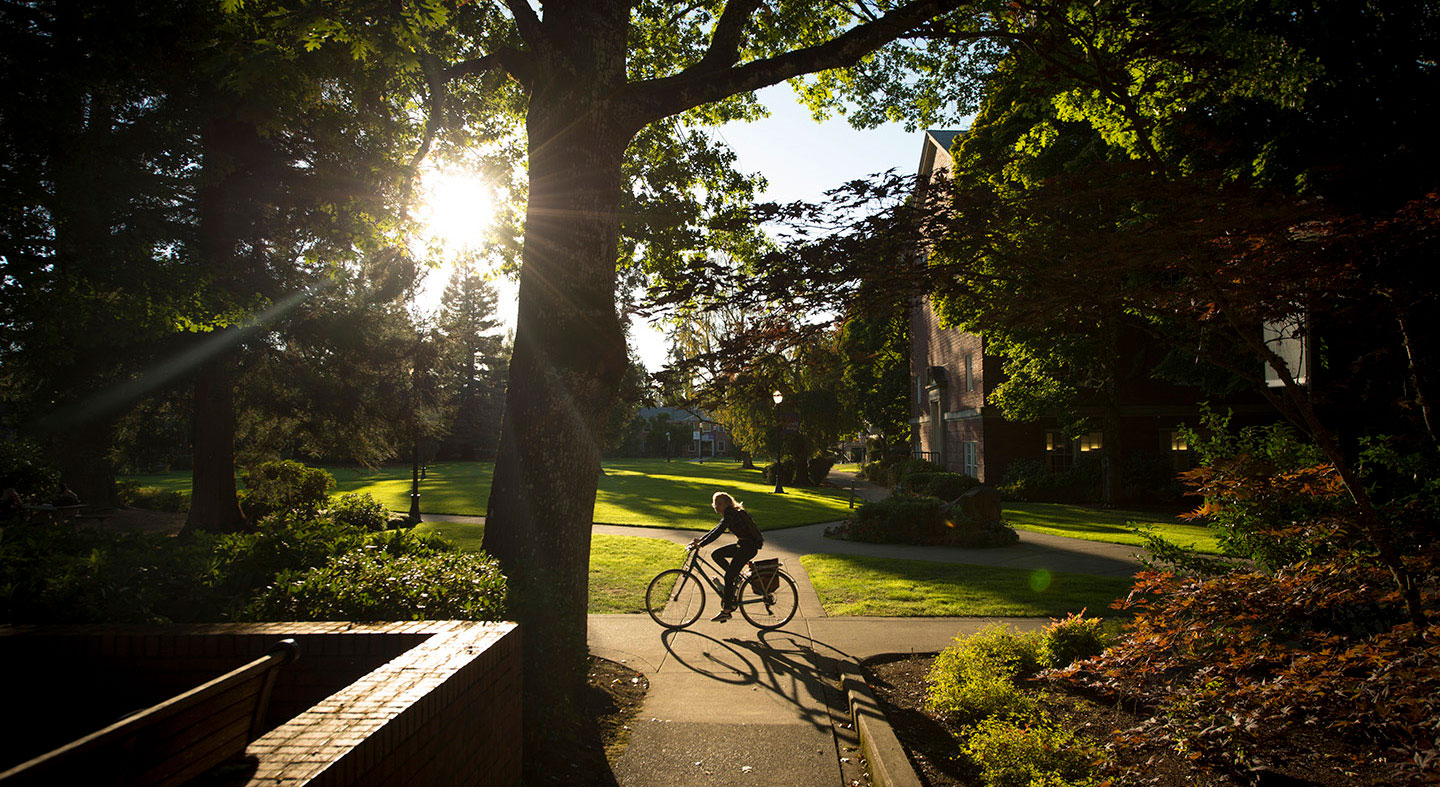 Student riding bike on path alongside Walker and Riley Halls.