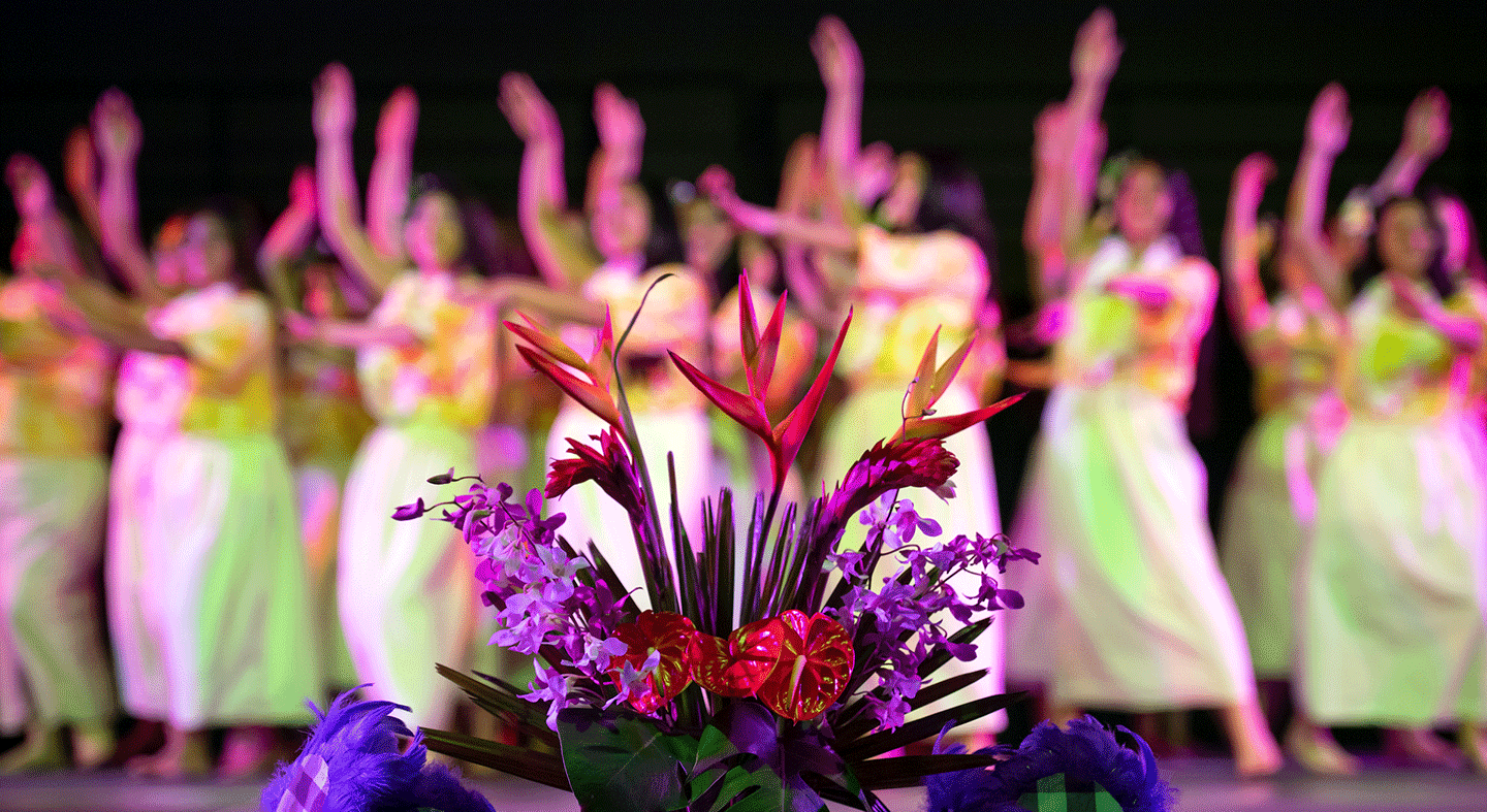 Ho'ike performers on stage with Hawaiian flowers in the foreground.