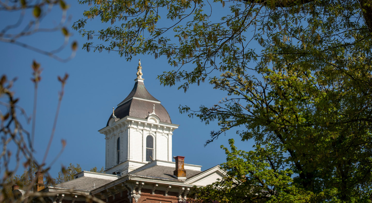 The top of Pioneer Hall between trees with a blue sky.