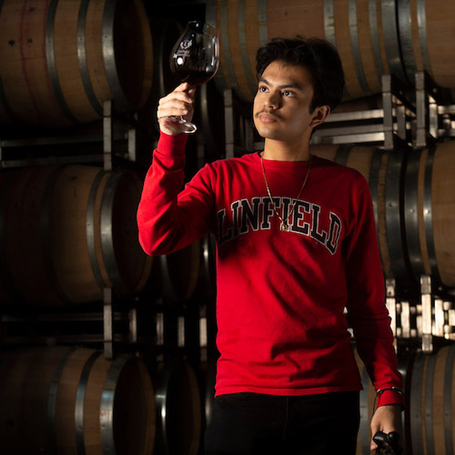 a wine studies student holding up a glass of Pinot with wine barrels in the background